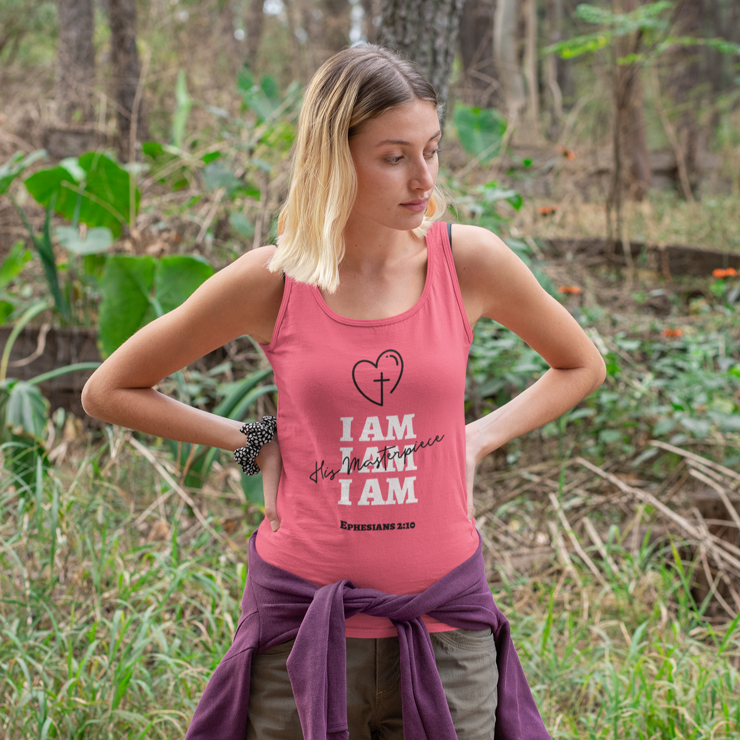 Woman wearing a pink tank top that says "I am his masterpiece" in a natural setting