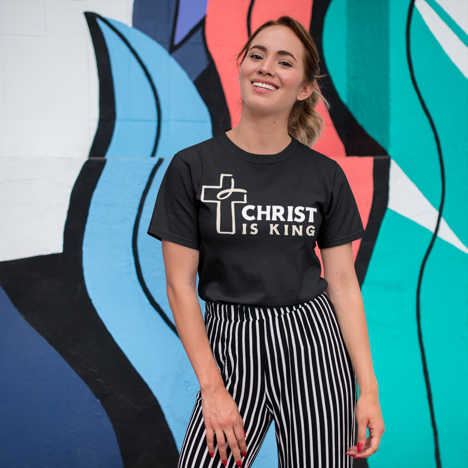 Person wearing a black t-shirt with 'Christ is King' text in front of a colorful mural.