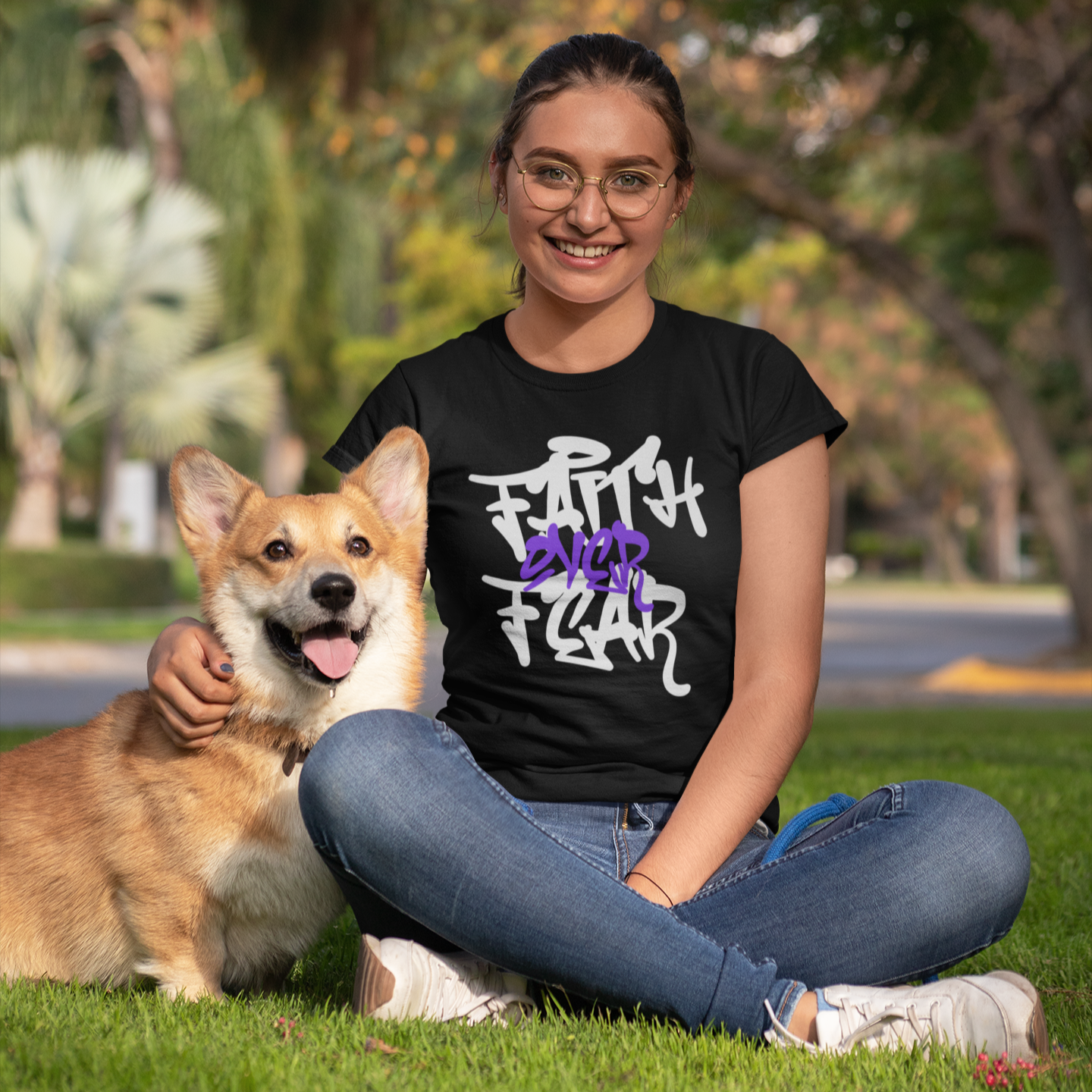 Woman sitting on grass with a dog, wearing a black t-shirt with white text.