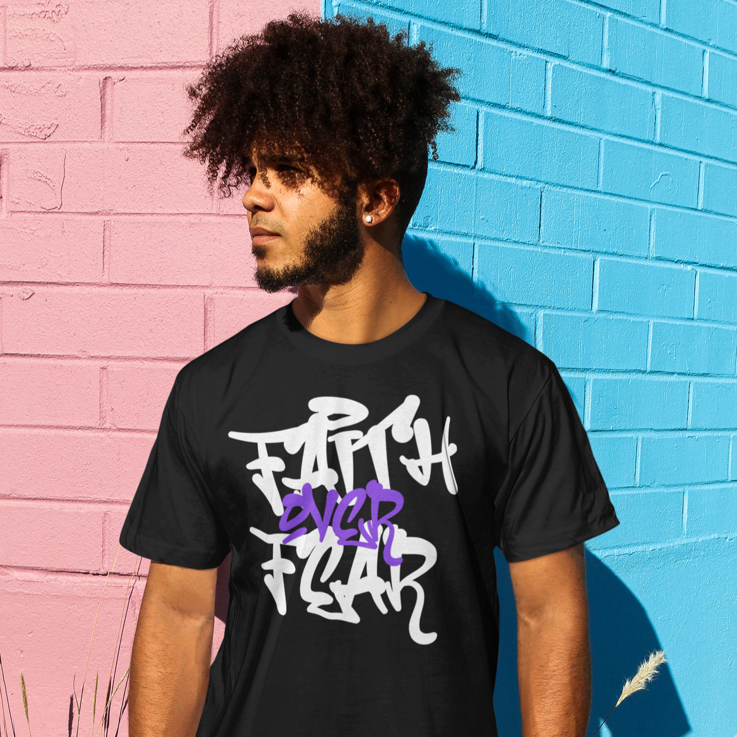 Person wearing a black t-shirt with 'Faith Over Fear' text in front of a colorful wall.