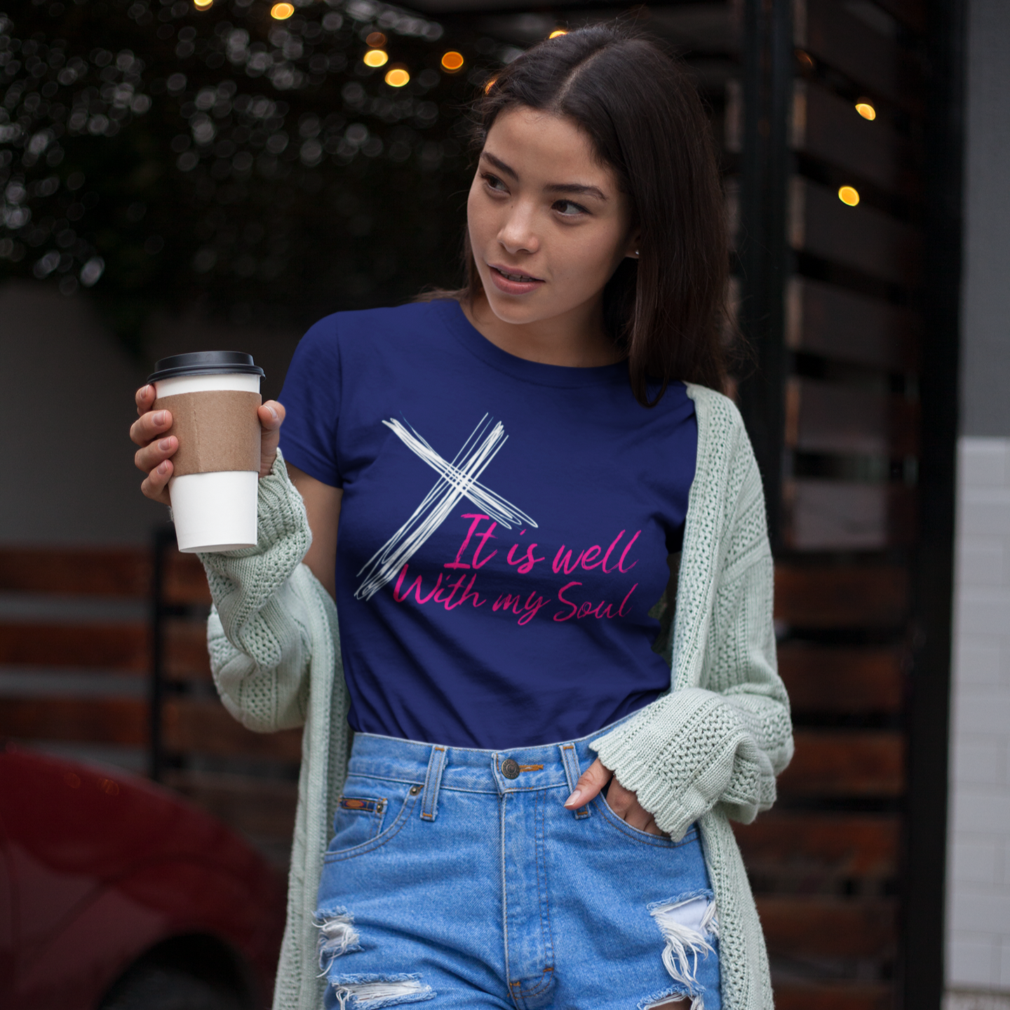 Woman wearing a blue t-shirt with text and holding a coffee cup outdoors.