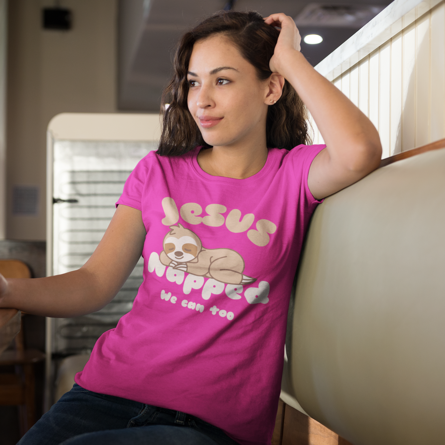 Woman in pink shirt with 'Jesus Hugged' design holding a coffee cup in a casual setting.