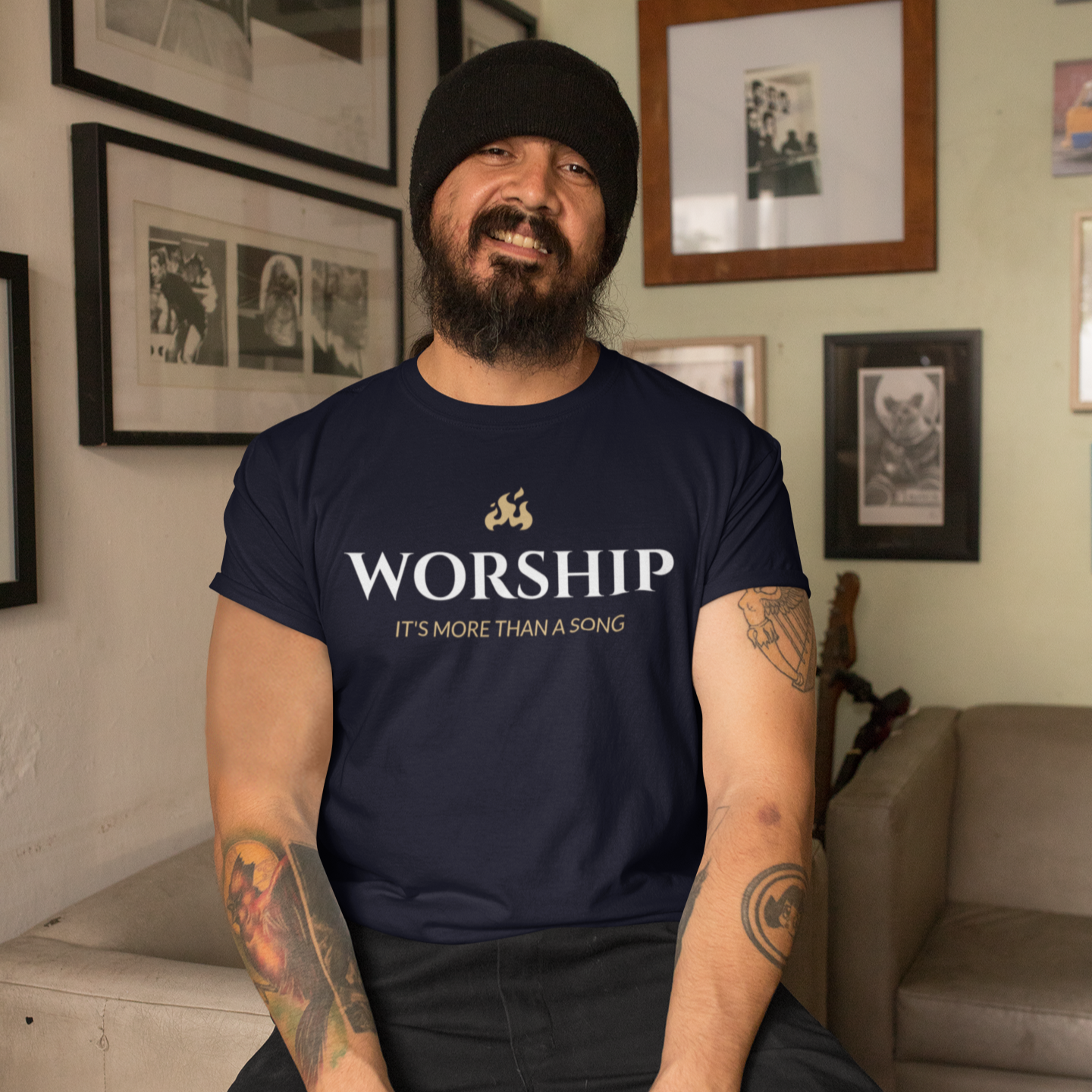 Man wearing a navy blue t-shirt with text, sitting in a room with framed pictures on the wall.